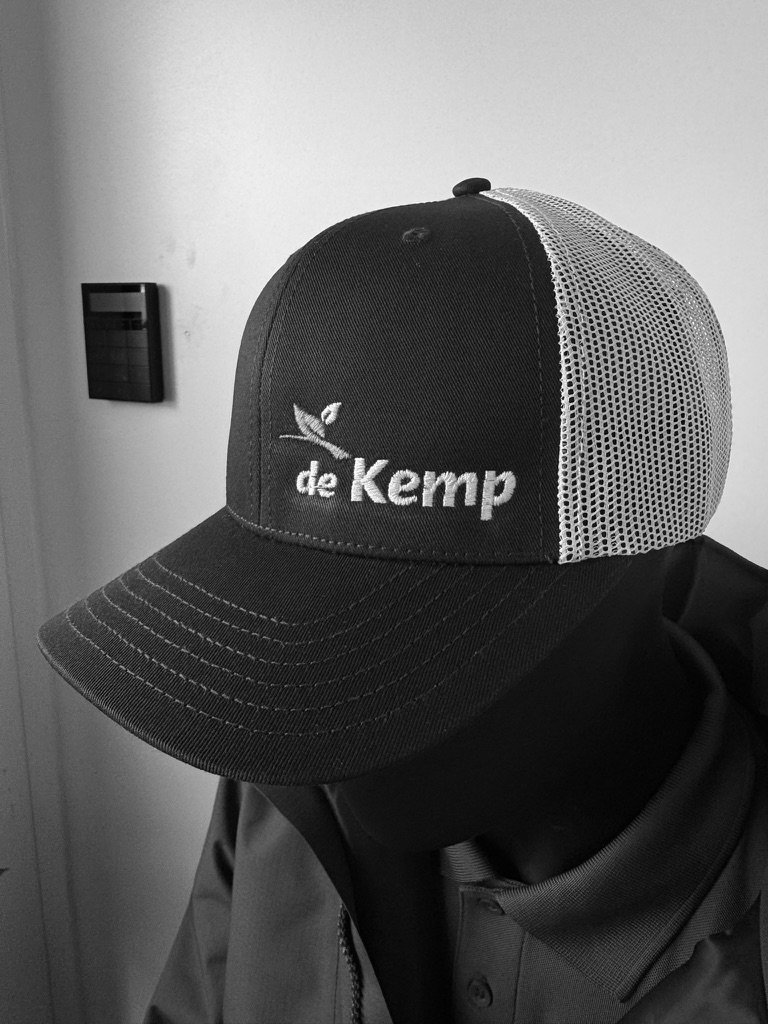 De Kemp logo geborduurd op de voorkant van een donkerblauwe trucker cap met wit mesh