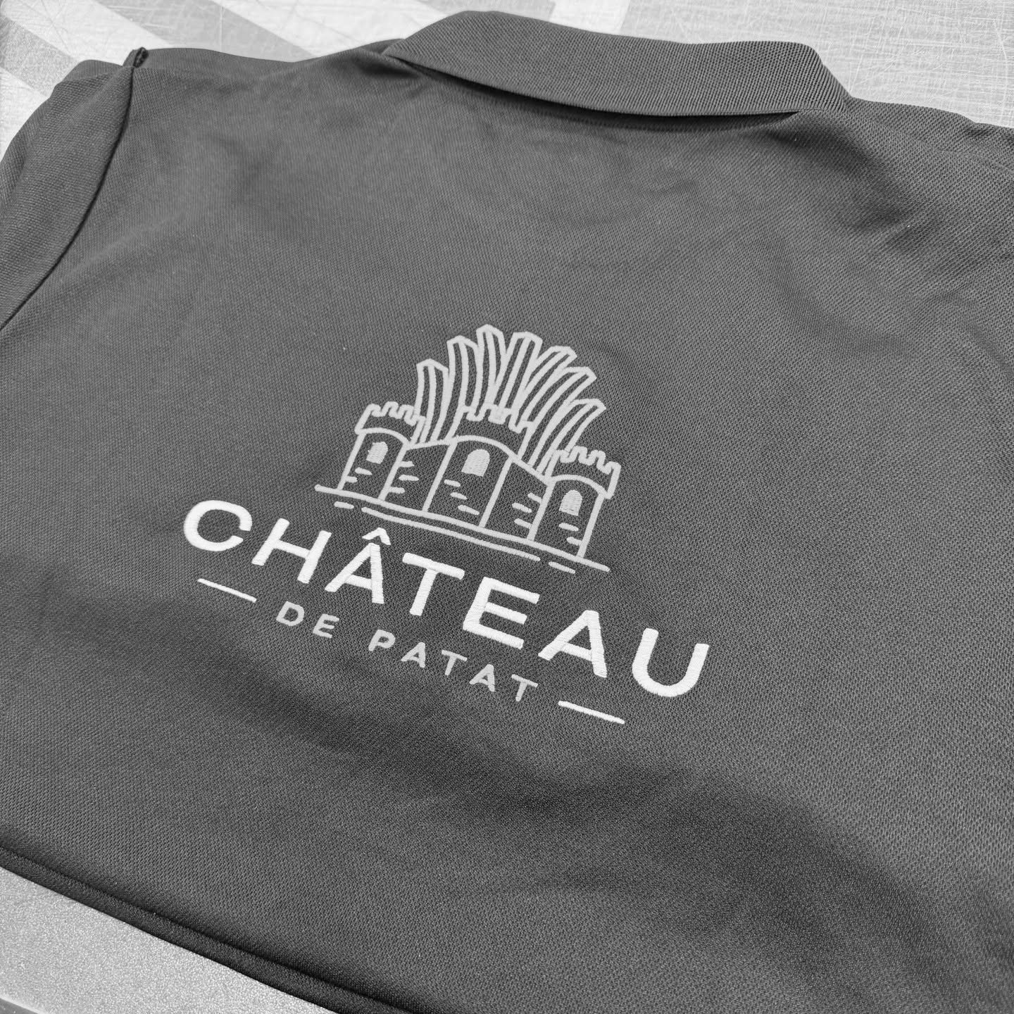 Château de Patat logo geborduurd op donkergrijze polo in wit en geel